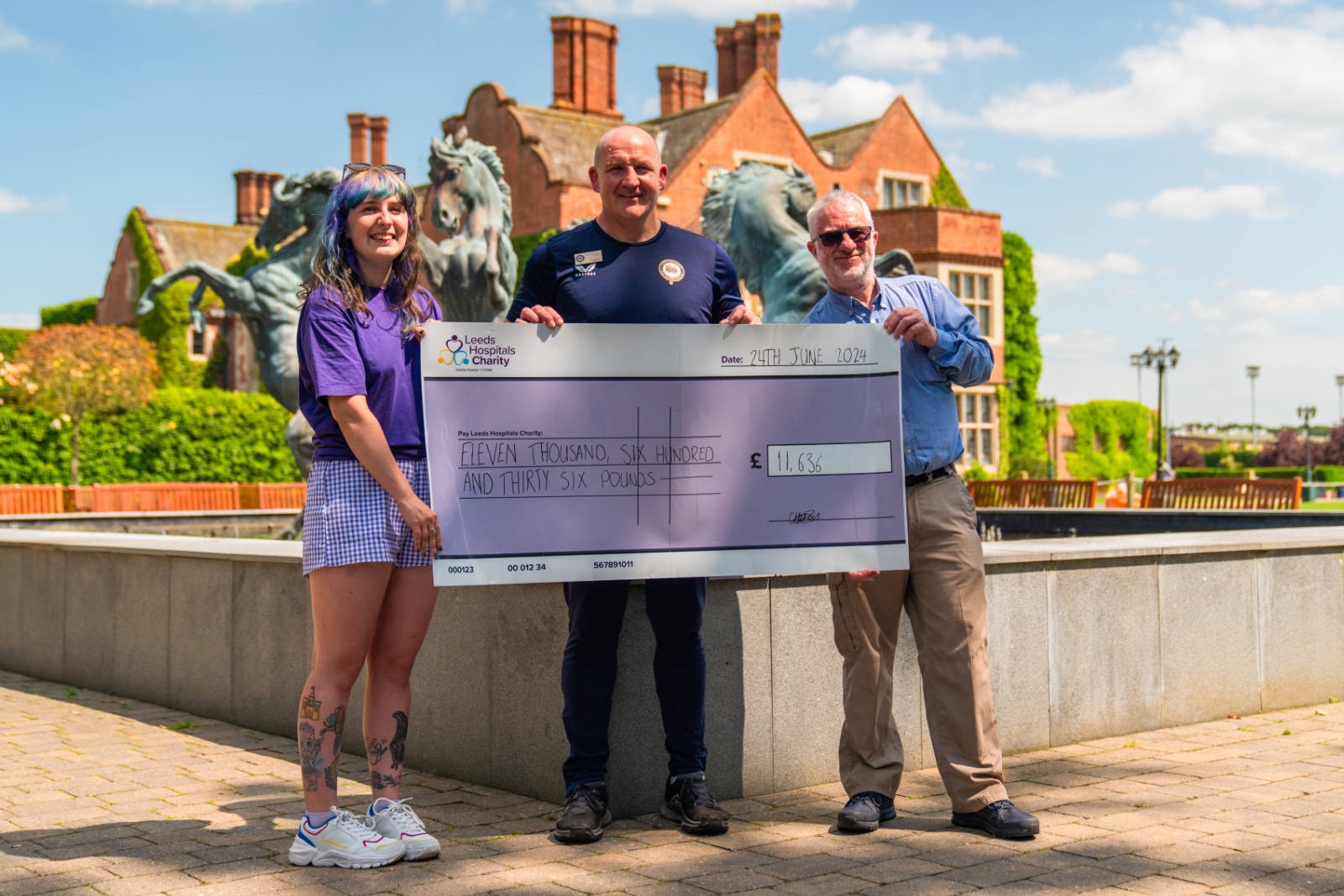 Rob Rawlinson, Head of Sport and David Payne, Head of English at Queen Ethelburga’s Collegiate present the final cheque from the fundraiser to Charlotte Bray from Leeds Hospitals Charity